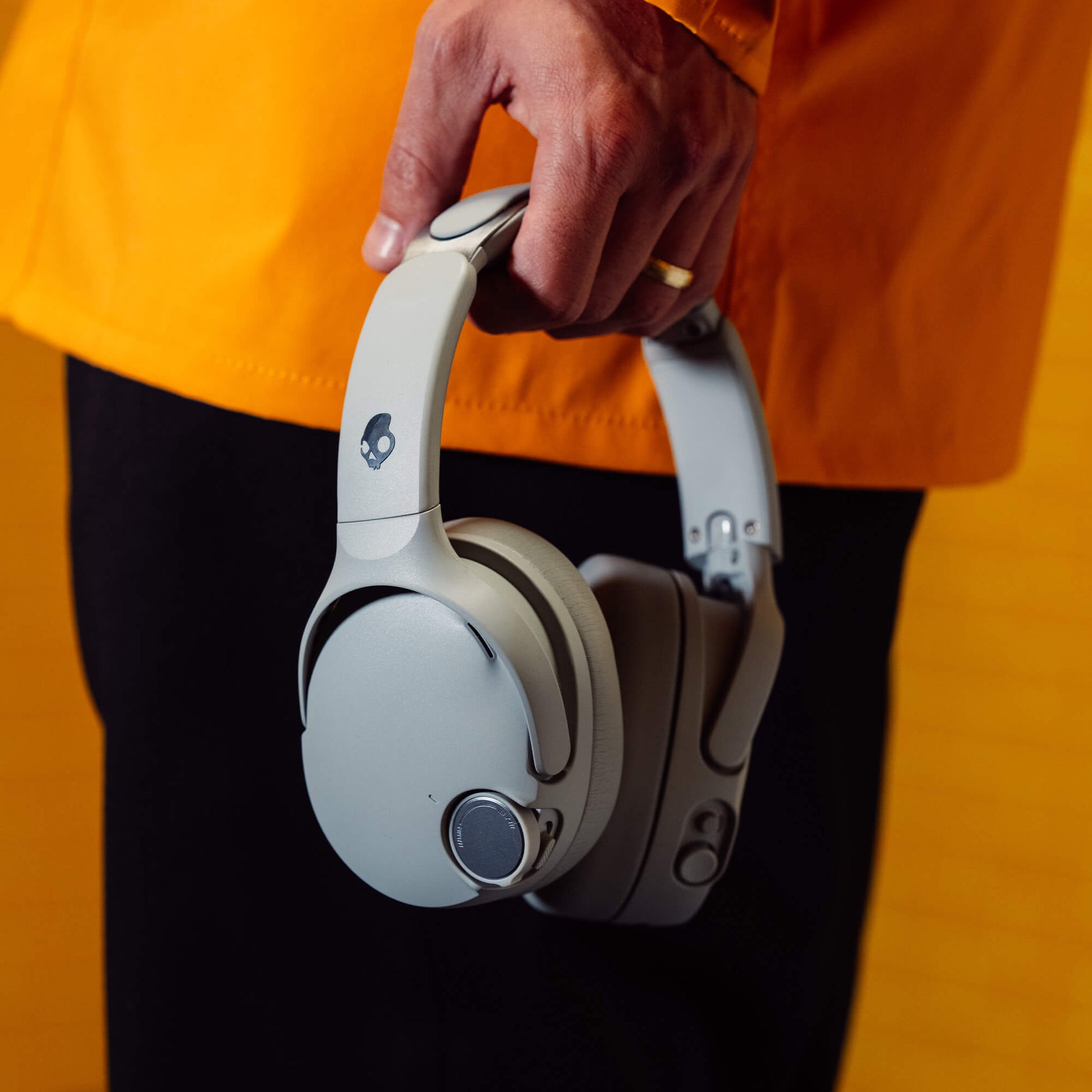 Grey Crusher 1080 ANC headphones held by a person wearing an orange jacket and black pants. | Cement