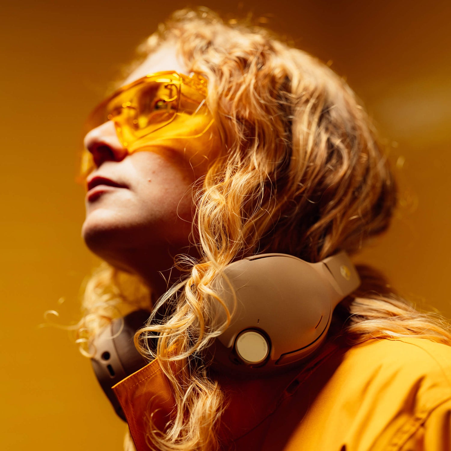 Person wearing Primer Crusher 1080 ANC Headphopnes with yellow sunglasses and headphones against a warm-toned background | Primer