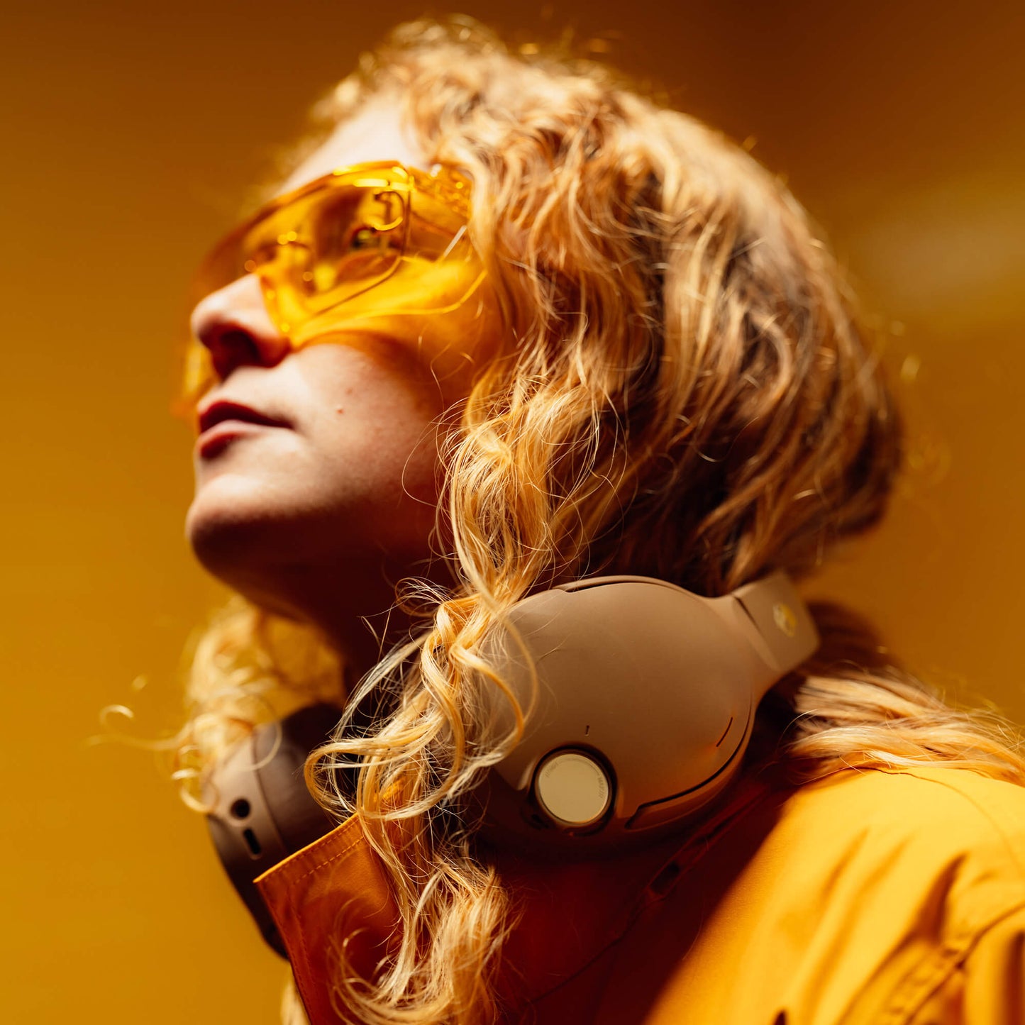 Person wearing Primer Crusher 1080 ANC Headphopnes with yellow sunglasses and headphones against a warm-toned background | Primer