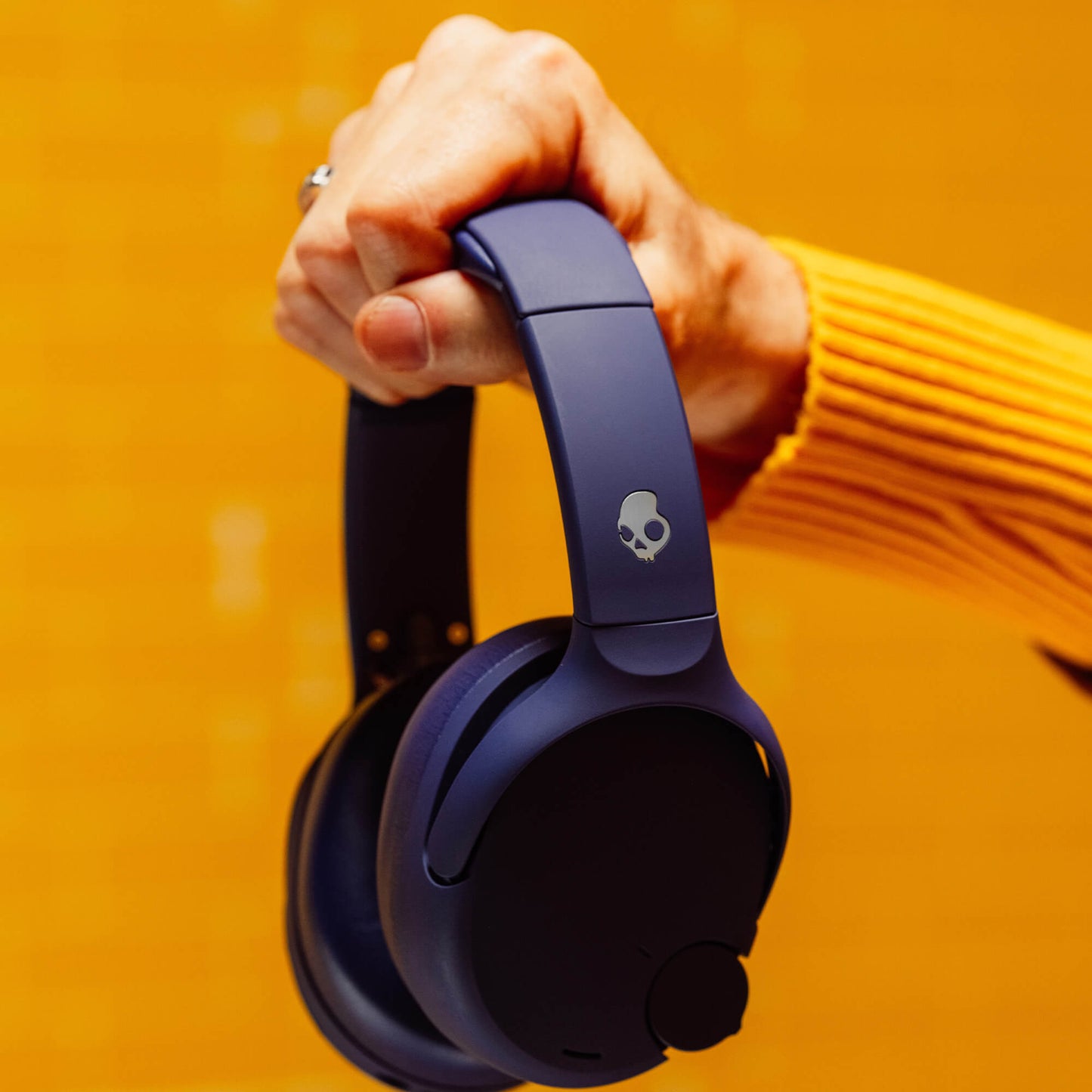 Person holding a pair of purple Crusher 720 headphones with a skull logo against an orange background | Future