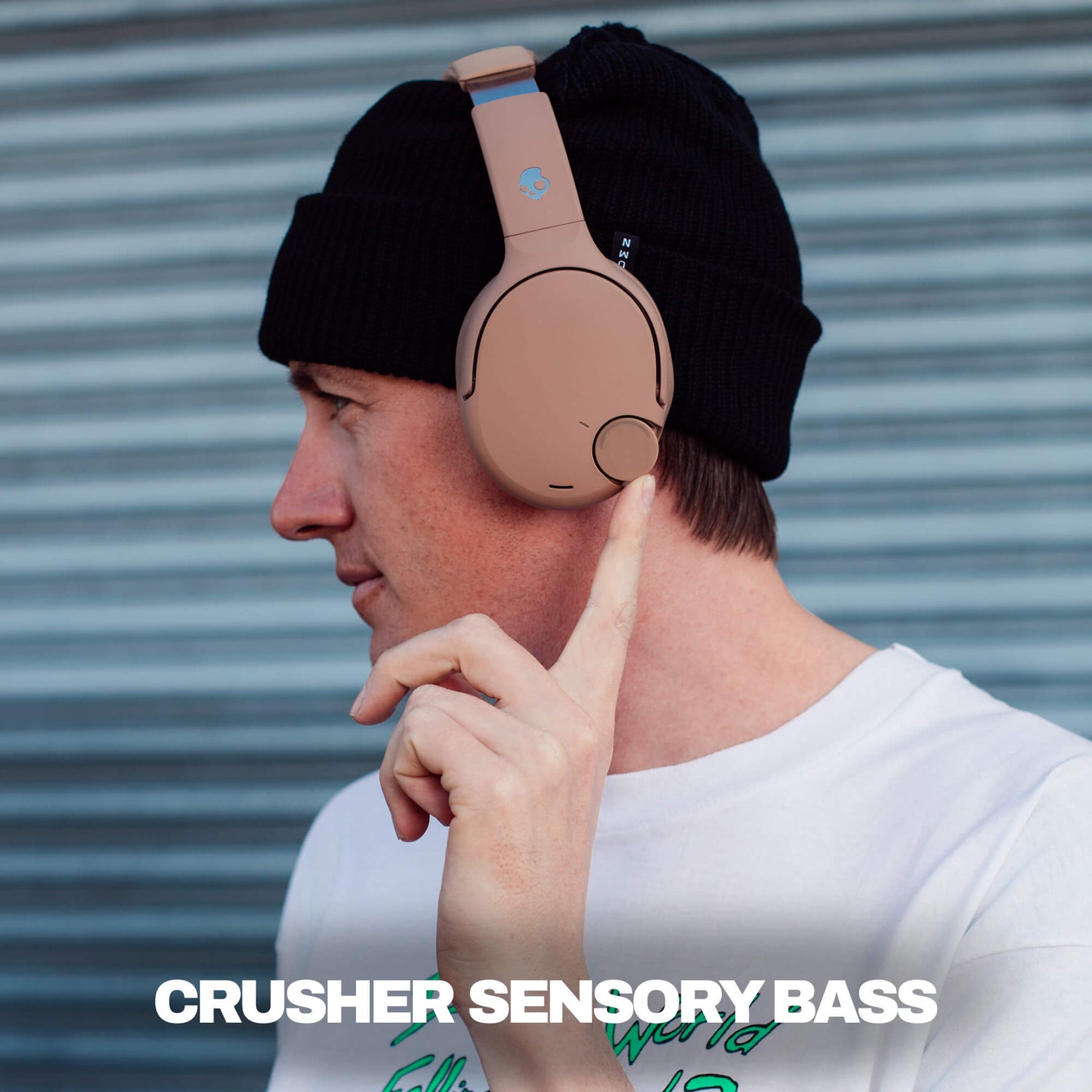 Person wearing a black beanie with brown Crusehr 720 headphones, pointing to the headphones, against a metallic background. | Primer