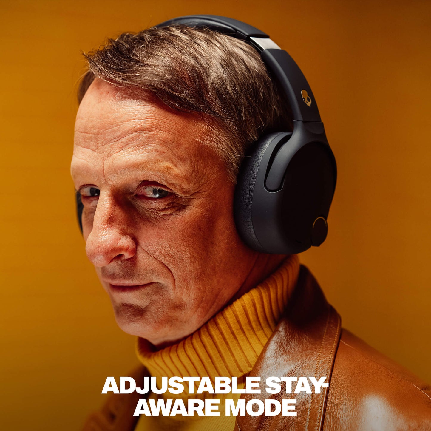 Tony Hawk wearing black Crusher 720 headphones with text 'Adjustable Stay Aware Mode' on a warm-toned background | True Black