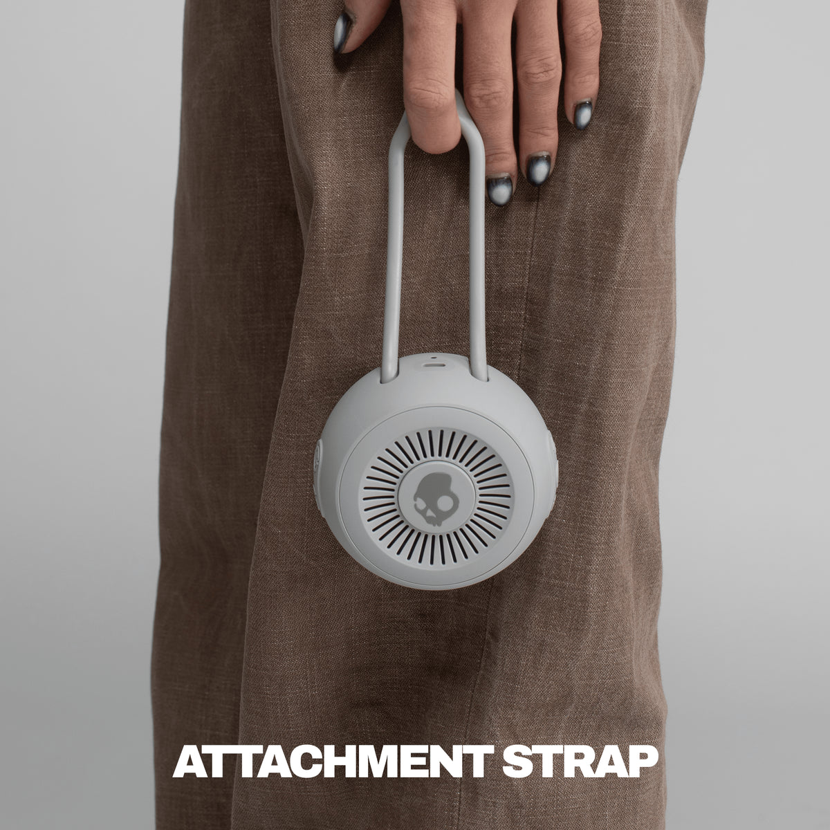 Gray attachment strap for speaker being held by someone with tan pants | Cement