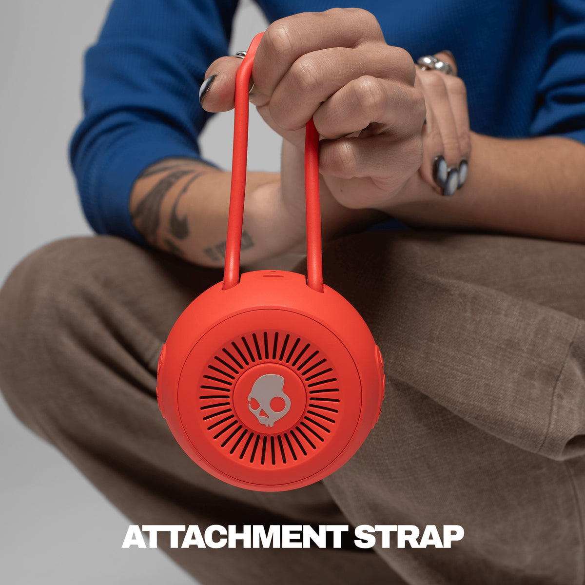 red attachment strap for speaker being held by someone with a blue shirt and tan pants | Plasma