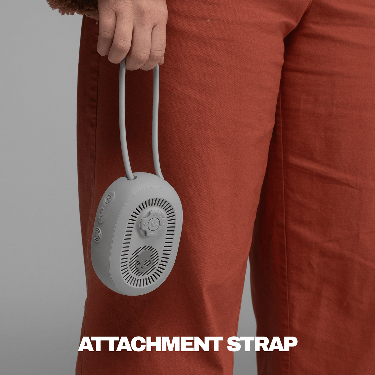 A close-up of a person wearing rust-colored pants holding a session 540 speaker by its attachment strap, with the text 'ATTACHMENT STRAP' at the bottom. | Cement