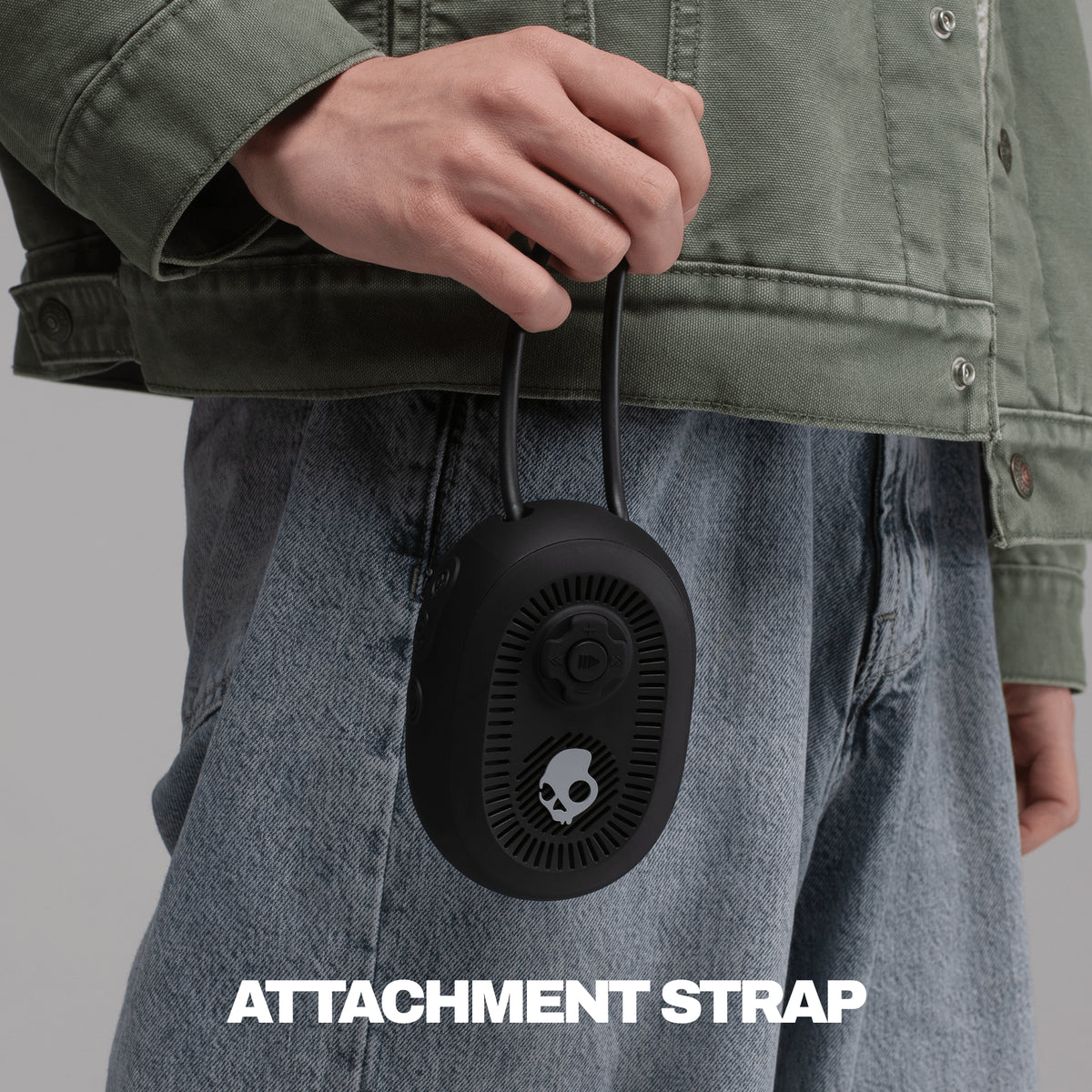 A person wearing an olive green jacket and blue jeans holds a black session 540 speaker with an attached black strap. | True Black