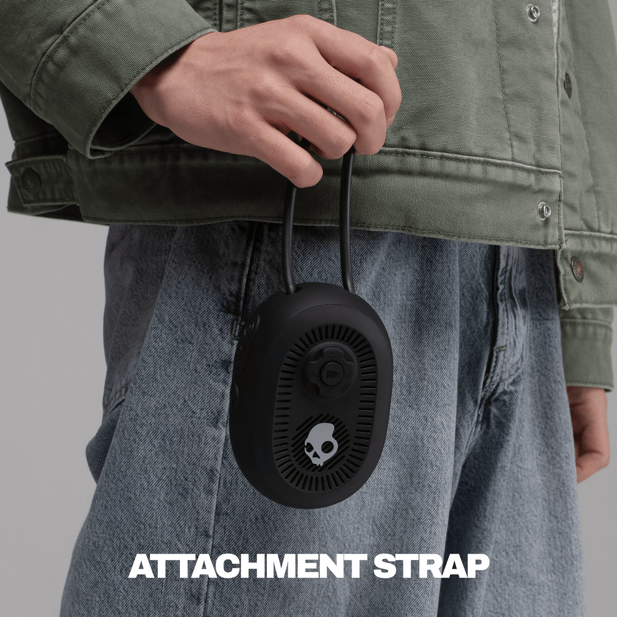 A person wearing an olive green jacket and blue jeans holds a black session 540 speaker with an attached black strap. | True Black