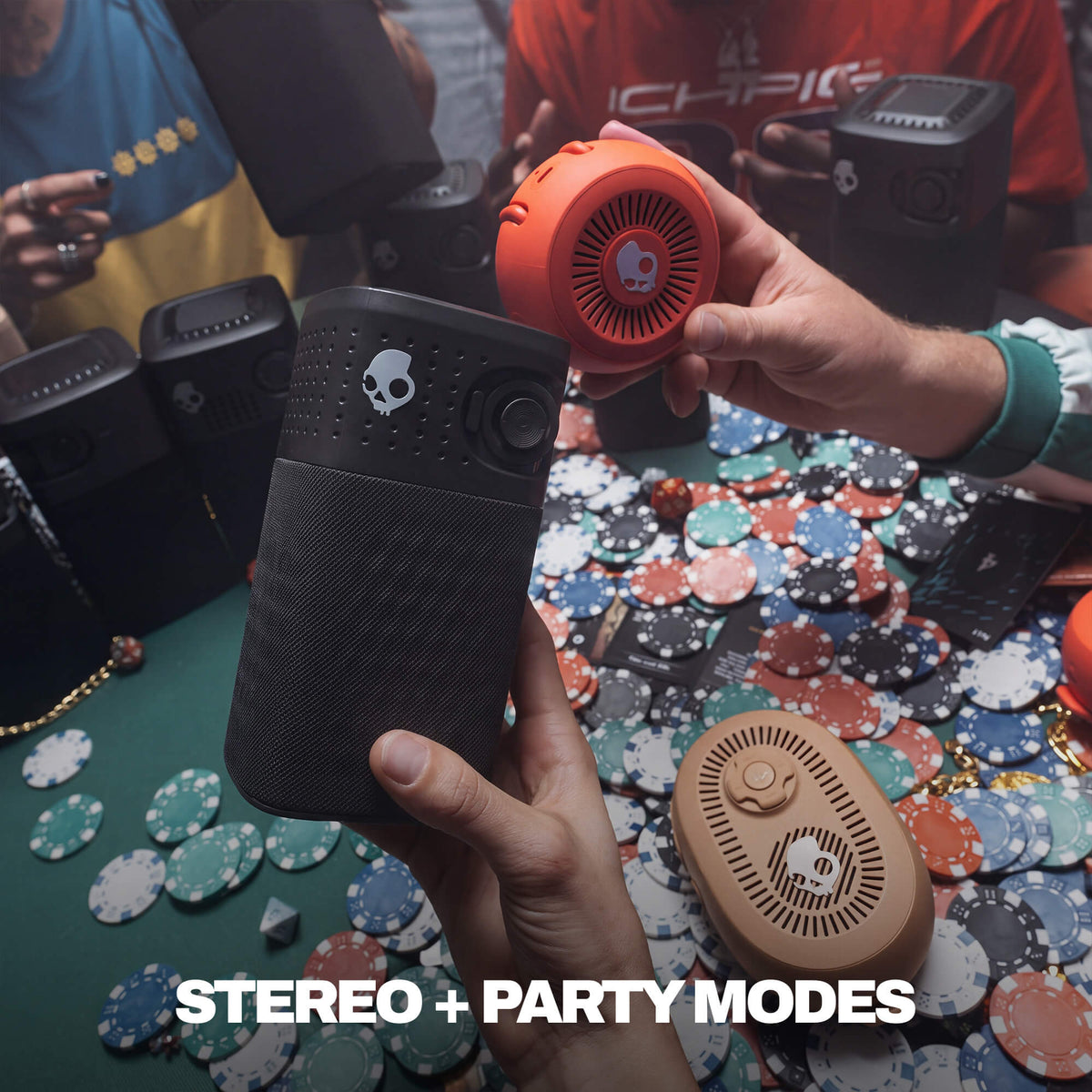 A person holds a black session 720 speaker in one hand and a session 360 speaker in the other over a table covered with poker chips. Other speakers and people are visible in the background, with the text 'STEREO + PARTY MODES' at the bottom. | True Black