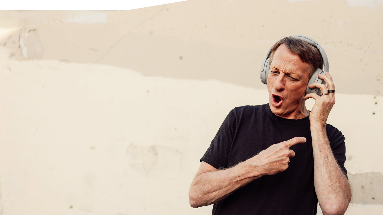 Man wearing headphones and pointing to his head with a neutral background