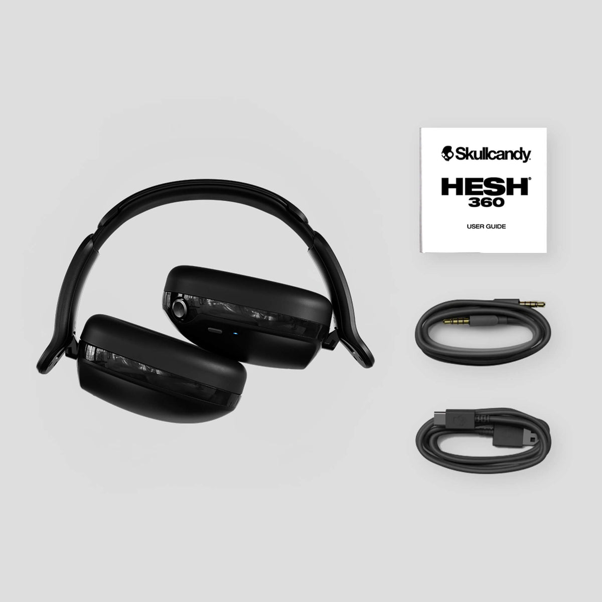 Black headphones with cables and Skullcandy HESH 360 user guide on a light gray background | True Black