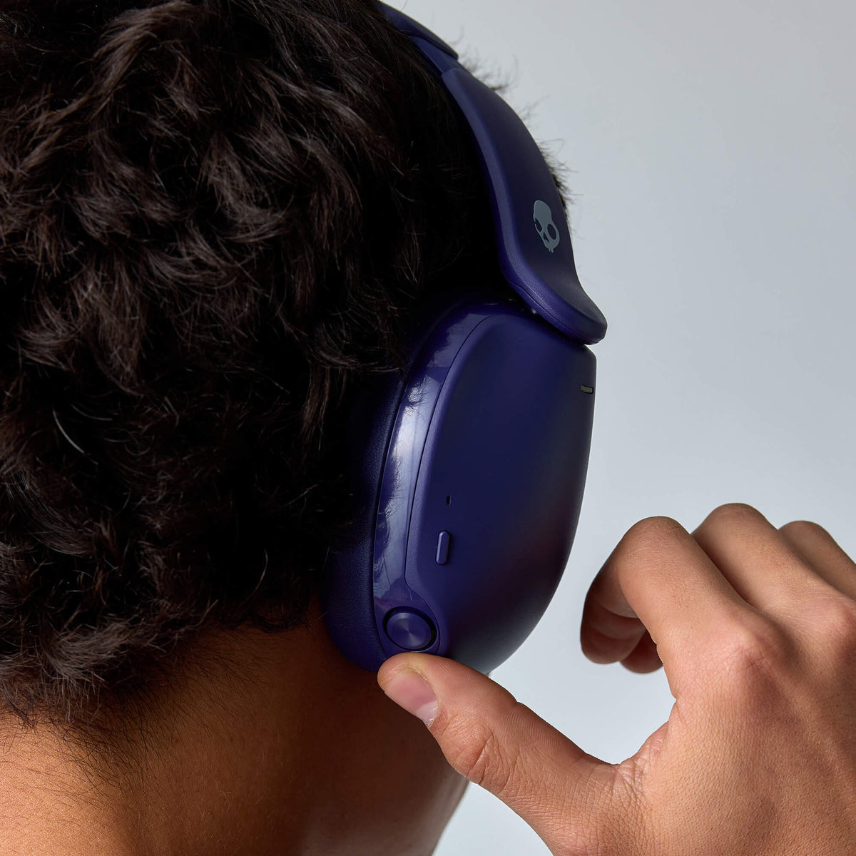 A close-up of a person wearing dark blue hesh 360 over-ear headphones and touching the side of the earcup, with a light gray background. | Future