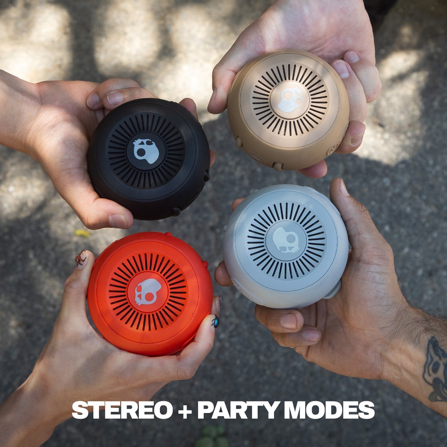 Four hands holding different colored round speakers with 'STEREO + PARTY MODES' text. | Cement