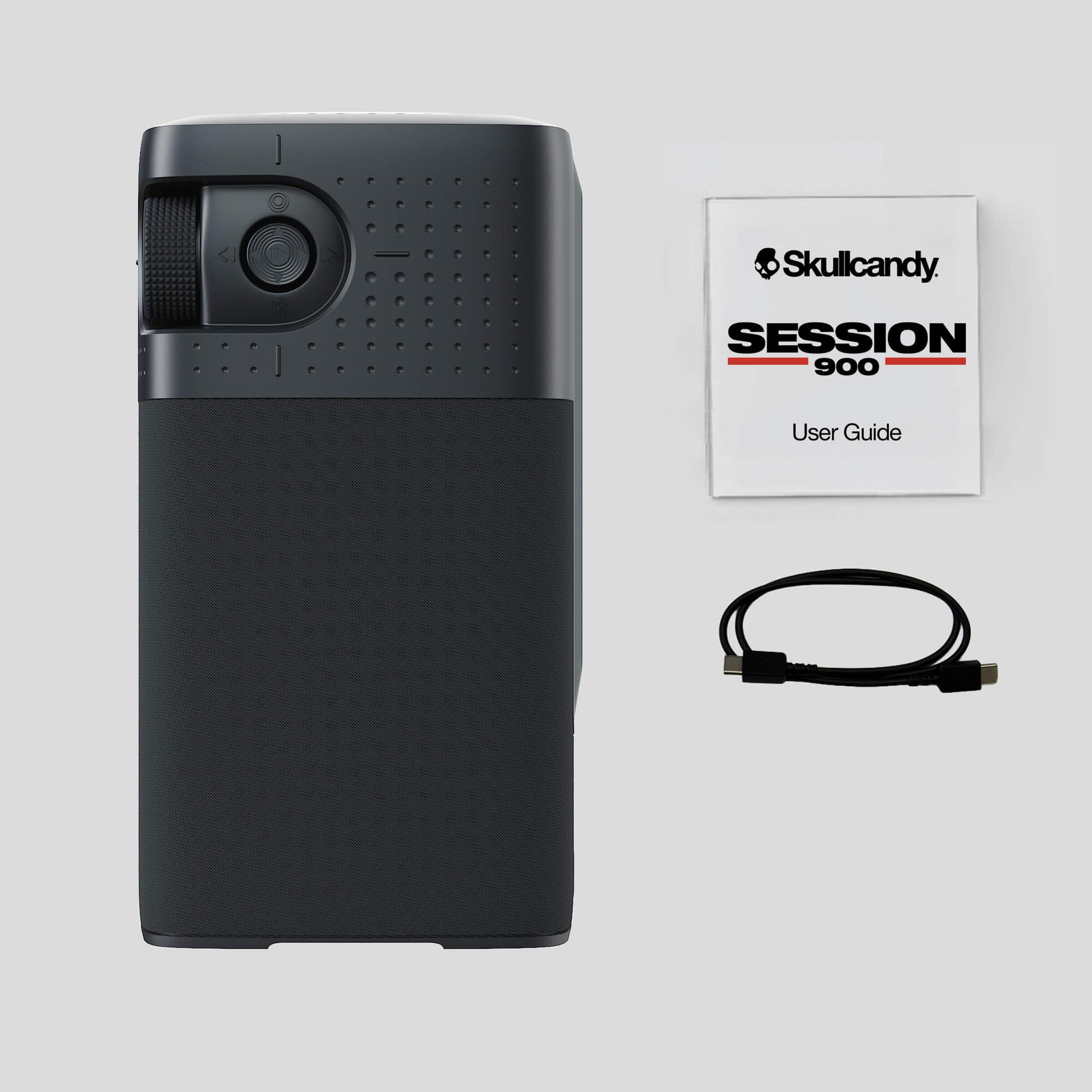 A black Skullcandy Session 900 portable speaker shown next to its user guide booklet and a black USB cable on a light gray background. | Cement