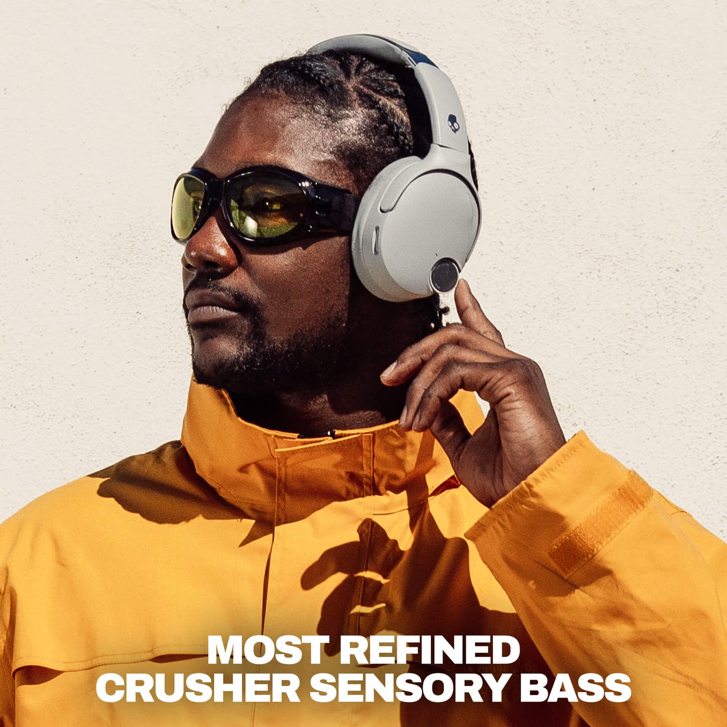 A man wearing white Crusher 1080 over-ear headphones and dark sunglasses, dressed in a bright yellow jacket, with the text 'MOST REFINED CRUSHER SENSORY BASS' at the bottom. | Cement