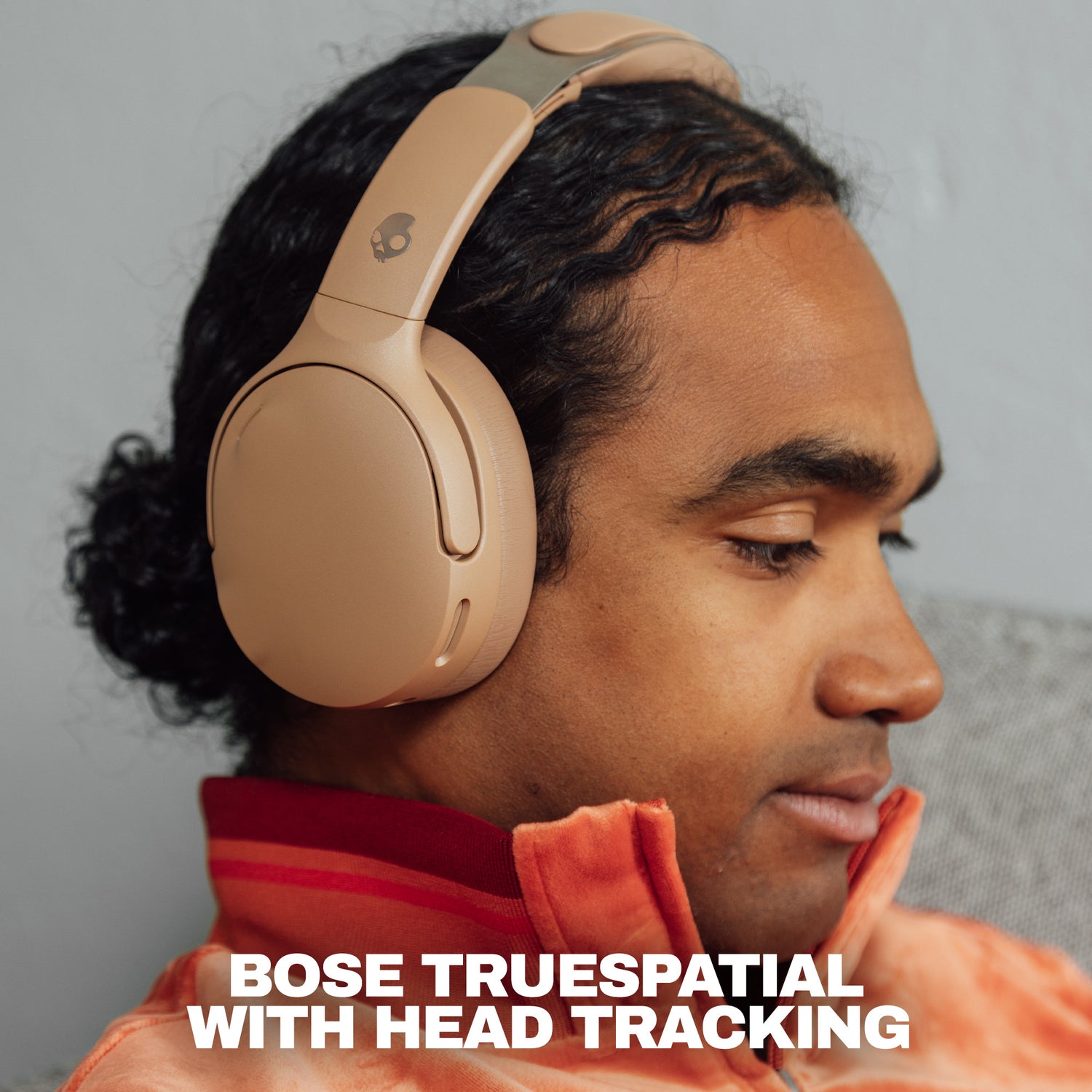 A man wearing beige Skullcandy 1080 with Bose TrueSpatial over-ear headphones with head tracking, shown in profile against a neutral gray background with promotional text at the bottom. | Primer