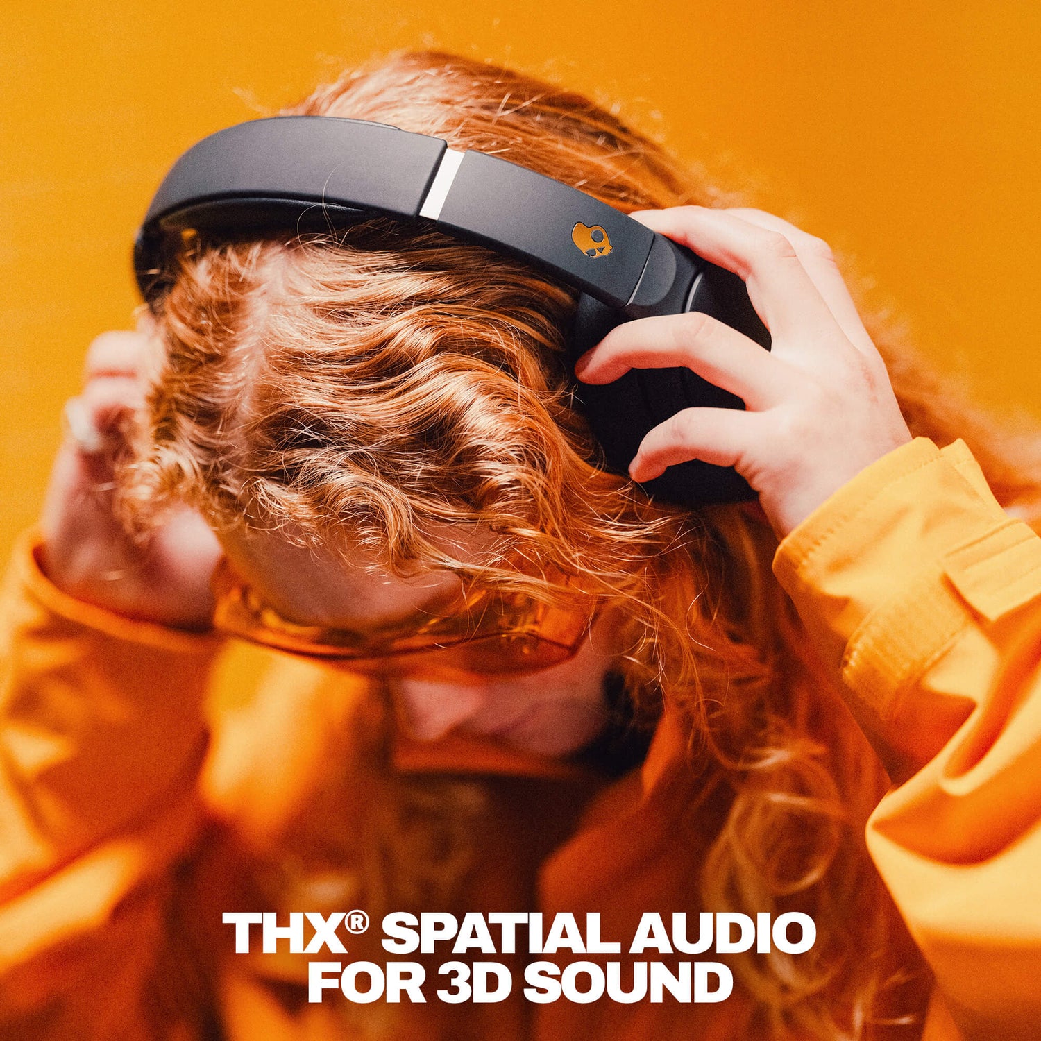 Person wearing black Crusher 720 headphones with THX Spatial Audio branding against an orange background | True Black