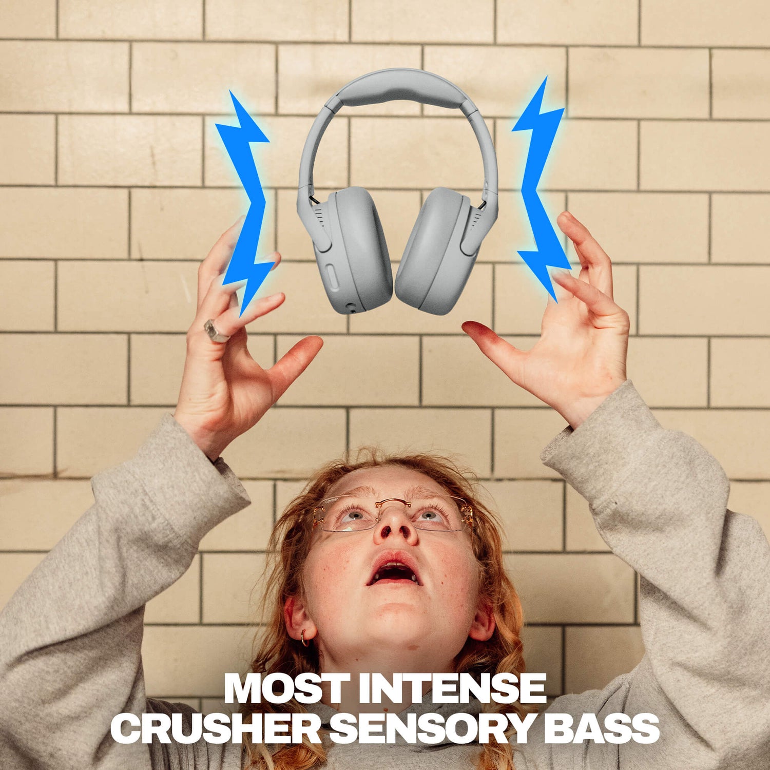 Person holding up Crusher 720 headphones with blue lightning bolts and 'MOST INTENSE CRUSHER SENSORY BASS' text against a tiled wall. | Cement